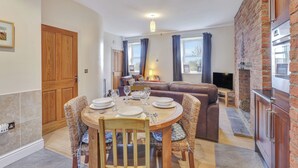 A dining area with a round table set for four, a brown leather sofa, and a kitchen area with a brick wall and wooden cabinets.