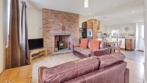 A living room with a brick fireplace, leather sofas, a TV, and a dining area with wooden cabinets.