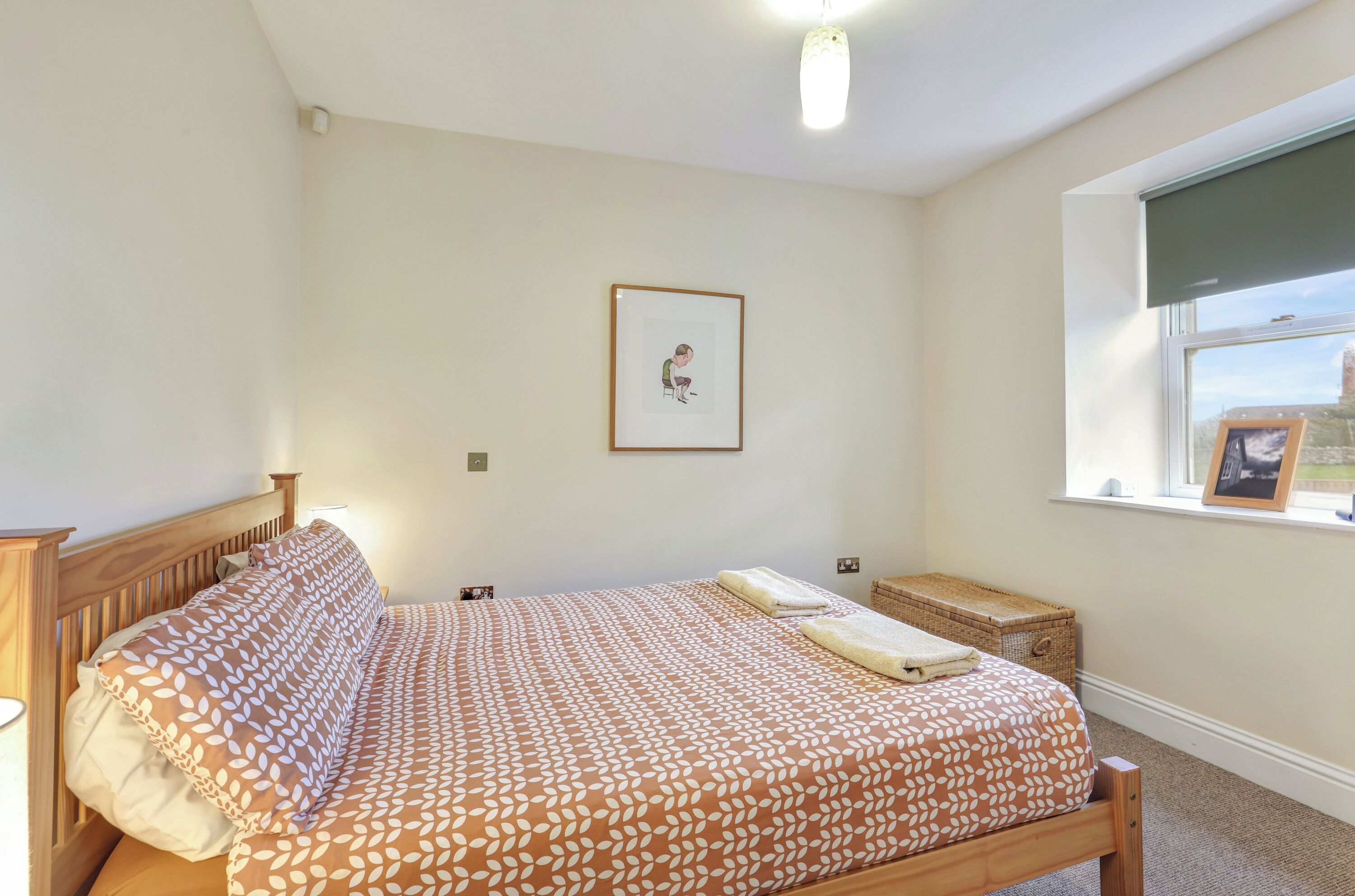 A bedroom with a bed, a bedside table, a window with a view, and a framed picture on the wall.