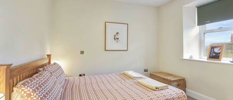 A bedroom with a bed, a bedside table, a window with a view, and a framed picture on the wall.