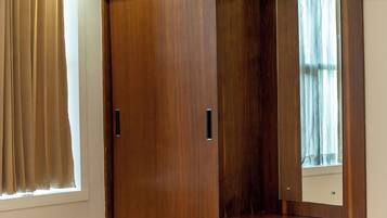 A hotel room with a large wooden wardrobe, a bed with a red and white bedspread, and a window with curtains.