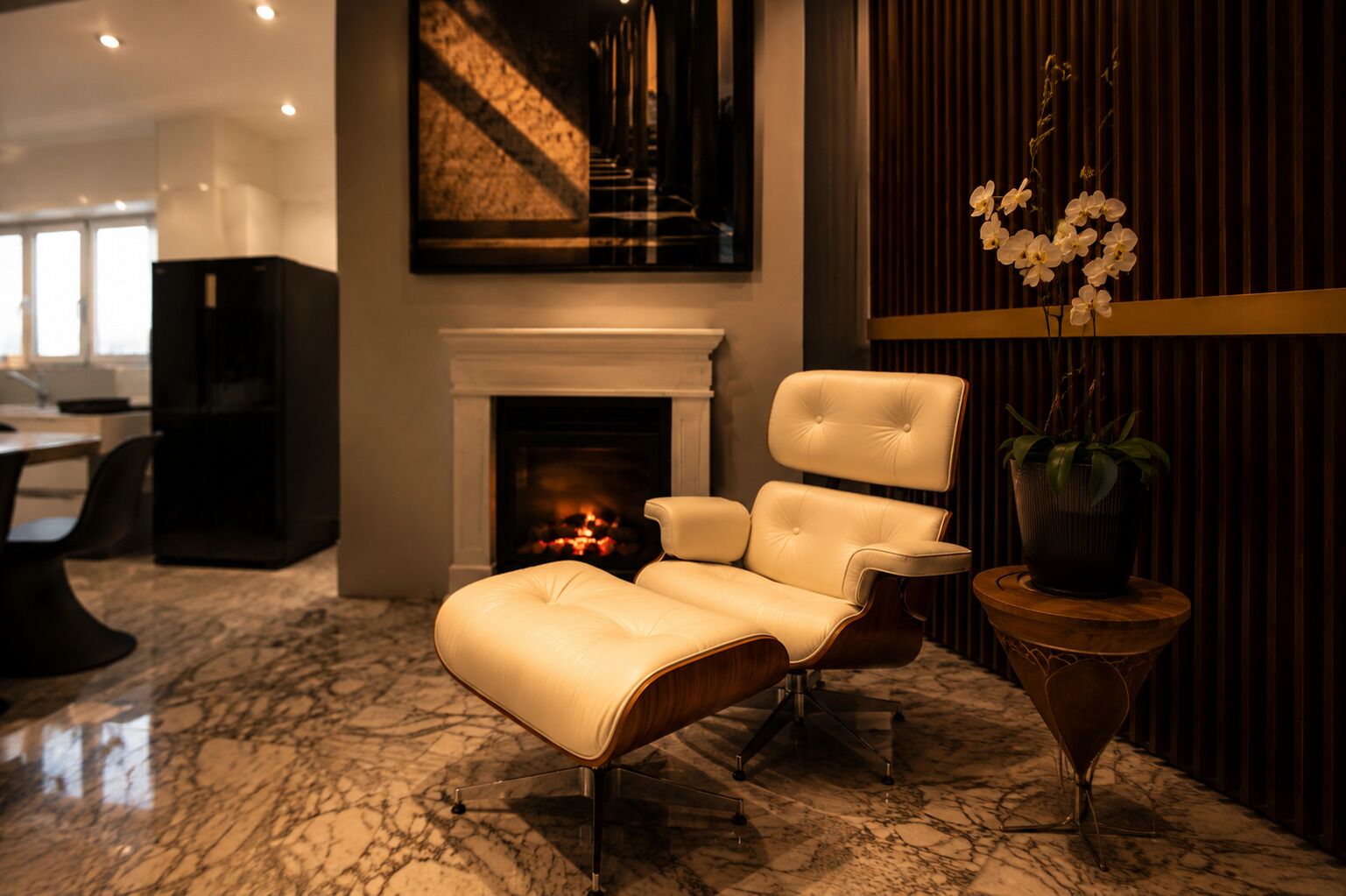 A lounge area with a fireplace, a comfortable lounge chair, a potted plant, and a marble floor.