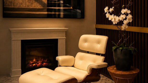 A modern living room with a fireplace, a leather armchair, a large abstract painting, and a potted orchid.