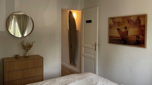 Un dormitorio con cama, cómoda, espejo, una tabla de surf en el pasillo y un cuadro en la pared.