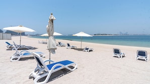A beach with sun loungers and umbrellas, a clear sky, and a calm sea.