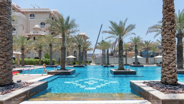 A swimming pool with palm trees and a building in the background.