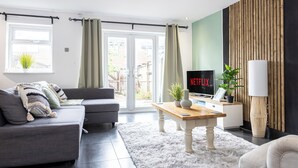 A modern living room with a grey sofa, a wooden coffee table, and a TV displaying 'NETFLIX'. - Relaxing 4BR Near City Centre  (Salford)