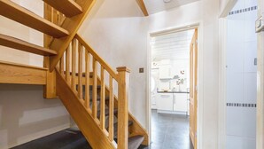 A wooden staircase leading to a kitchen area with white cabinets and a tiled floor. - Relaxing 4BR Near City Centre  (Salford)