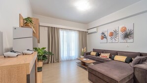 A modern living room with a sofa, a coffee table, a TV, and a kitchen area with a fridge and a plant. - Residence City Retreat (Rodos)
