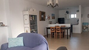 A spacious living area with a sofa, a dining table with chairs, a chandelier, and a kitchen area in the background. - A corner of paradise, surrounded by a majestic olive grove, 5 minutes from the beach. (Midoun)