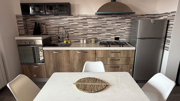 A modern kitchen with a central island, white chairs, and a dining table. - Daniel Apartment (Unknown)