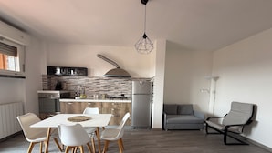 A modern kitchen with a dining area, featuring a herringbone tile backsplash, stainless steel appliances, and a dining table with chairs. - Daniel Apartment (Unknown)