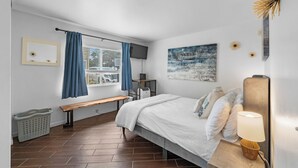 Ein Schlafzimmer mit Bett, Sitzbank, Fernseher und einem Fenster mit Vorhängen.