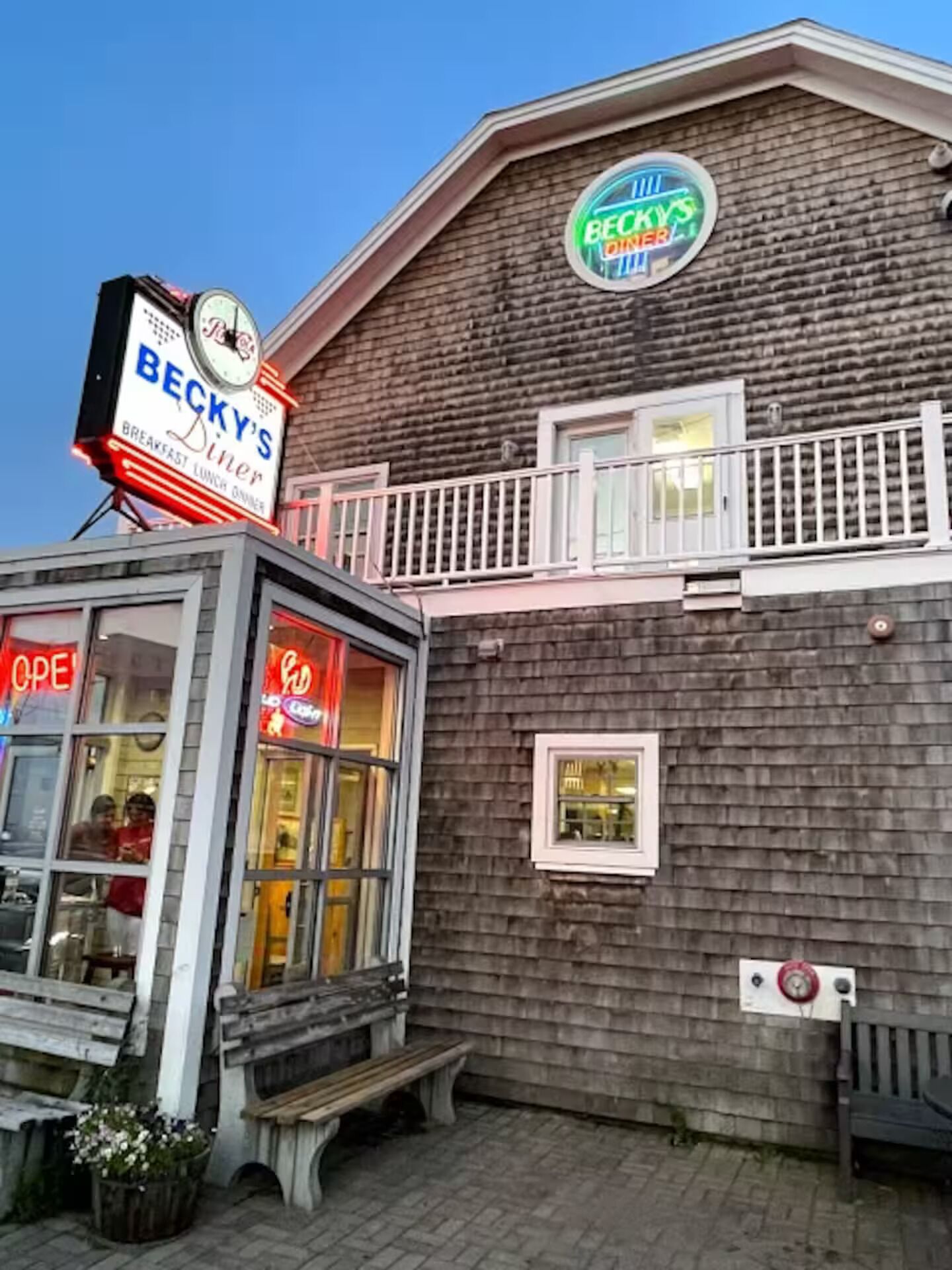 Un bâtiment avec une enseigne indiquant « Becky's Diner » et une horloge. On y trouve un banc et un bac à fleurs.
