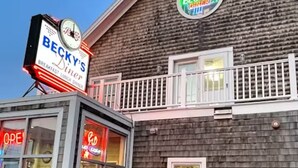 A building with a sign for 'Becky's Diner' and a clock. There is a bench and a planter with flowers. - Beautiful Back Cove Area/ "Maine the Way Life Should Be" (Portland)