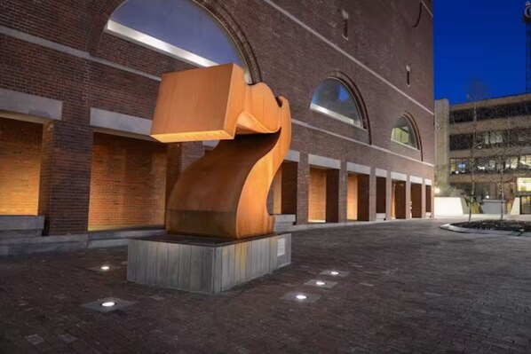 An outdoor area with a modern sculpture, brick building, and a paved walkway.