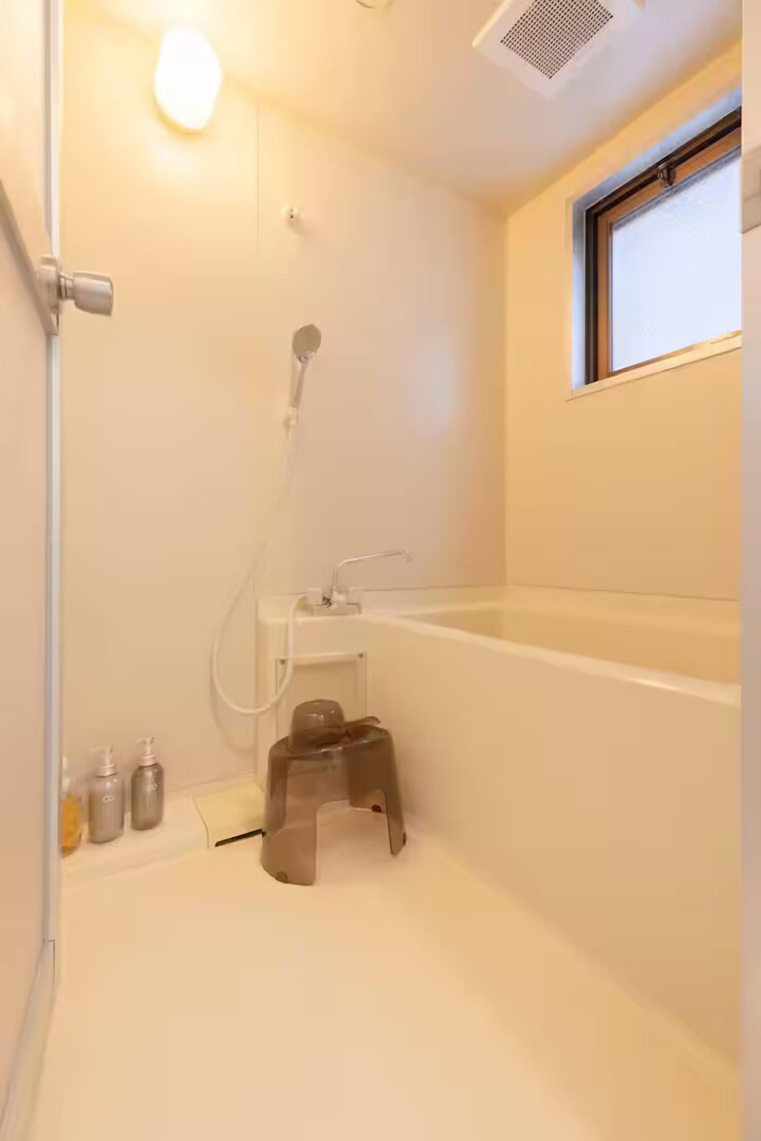 A minimalist bathroom with a bathtub, a shower, and a small stool.