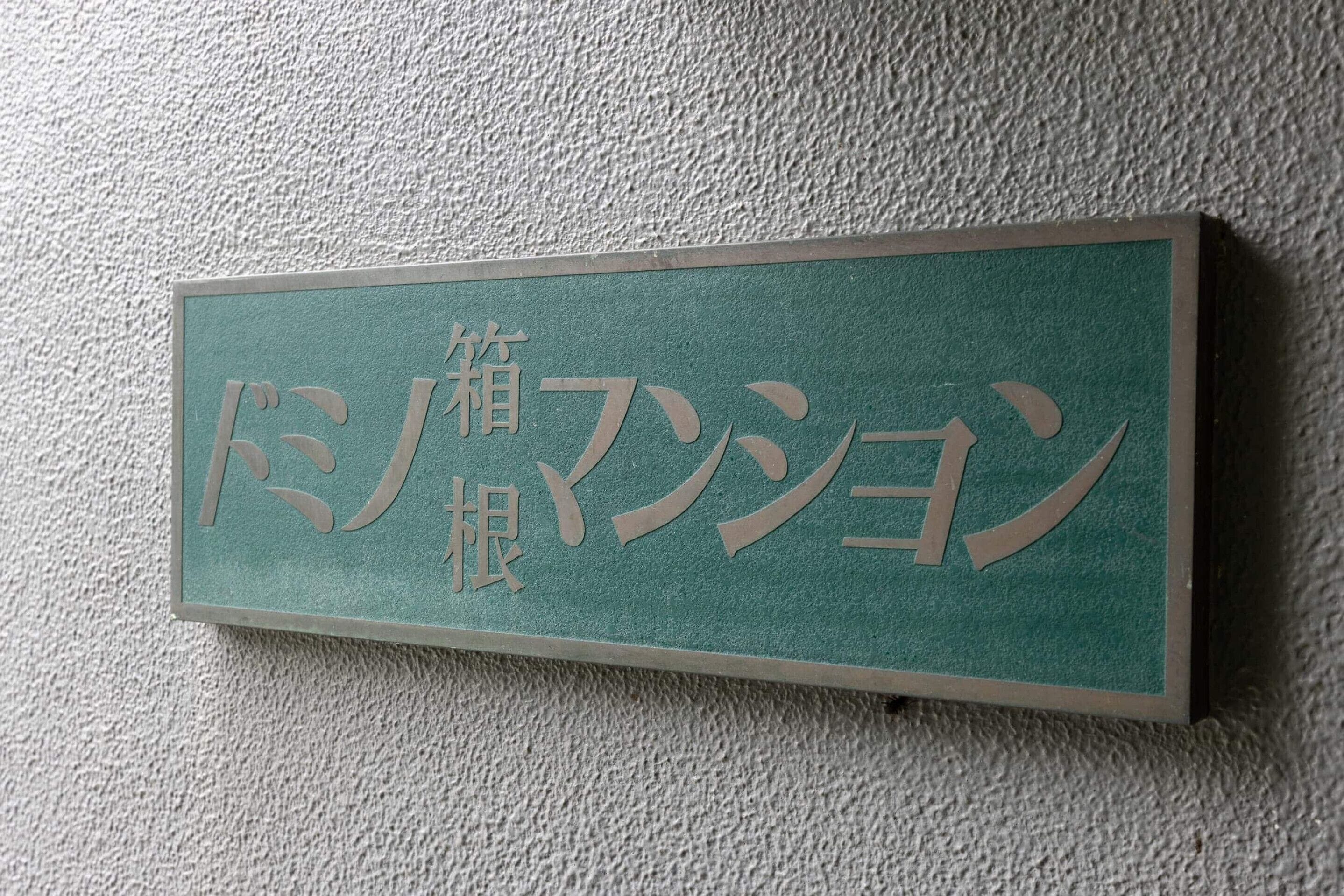 A rectangular sign with Japanese characters on a textured wall.