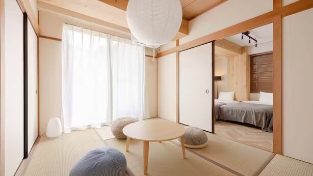 A traditional Japanese-style room with tatami flooring, a low wooden table, and a bed with a gray blanket.