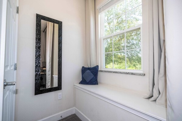 A bathroom with a window, a mirror, and a blue pillow on a ledge.