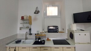 Eine kleine Küche mit Spüle, Herd und Mikrowelle. Über dem Herd befindet sich ein Fenster und rechts eine kleine Kühlbox.