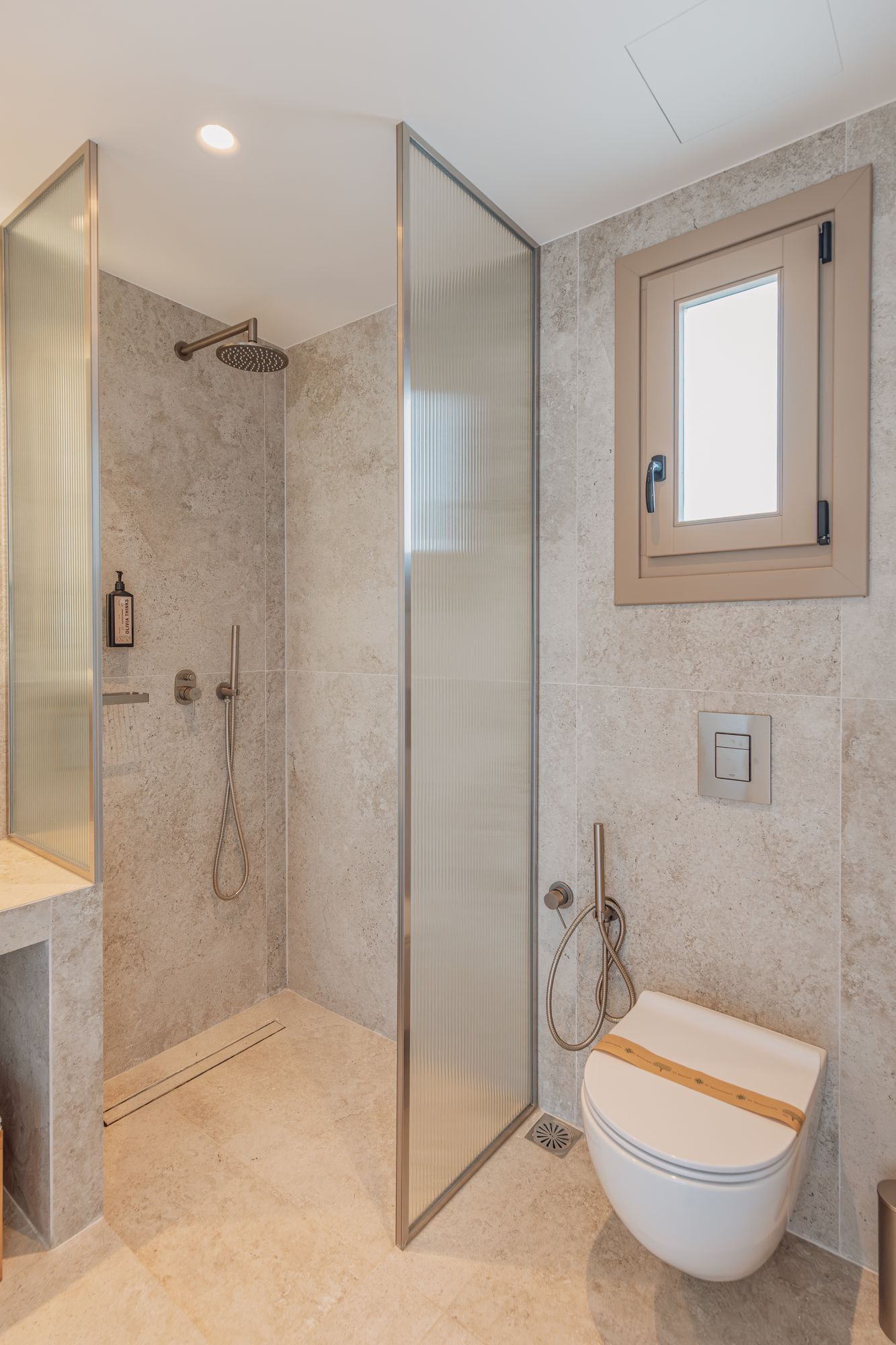 A modern bathroom with a glass-enclosed shower, a white sink with a gold trim, and a large mirror above the sink.