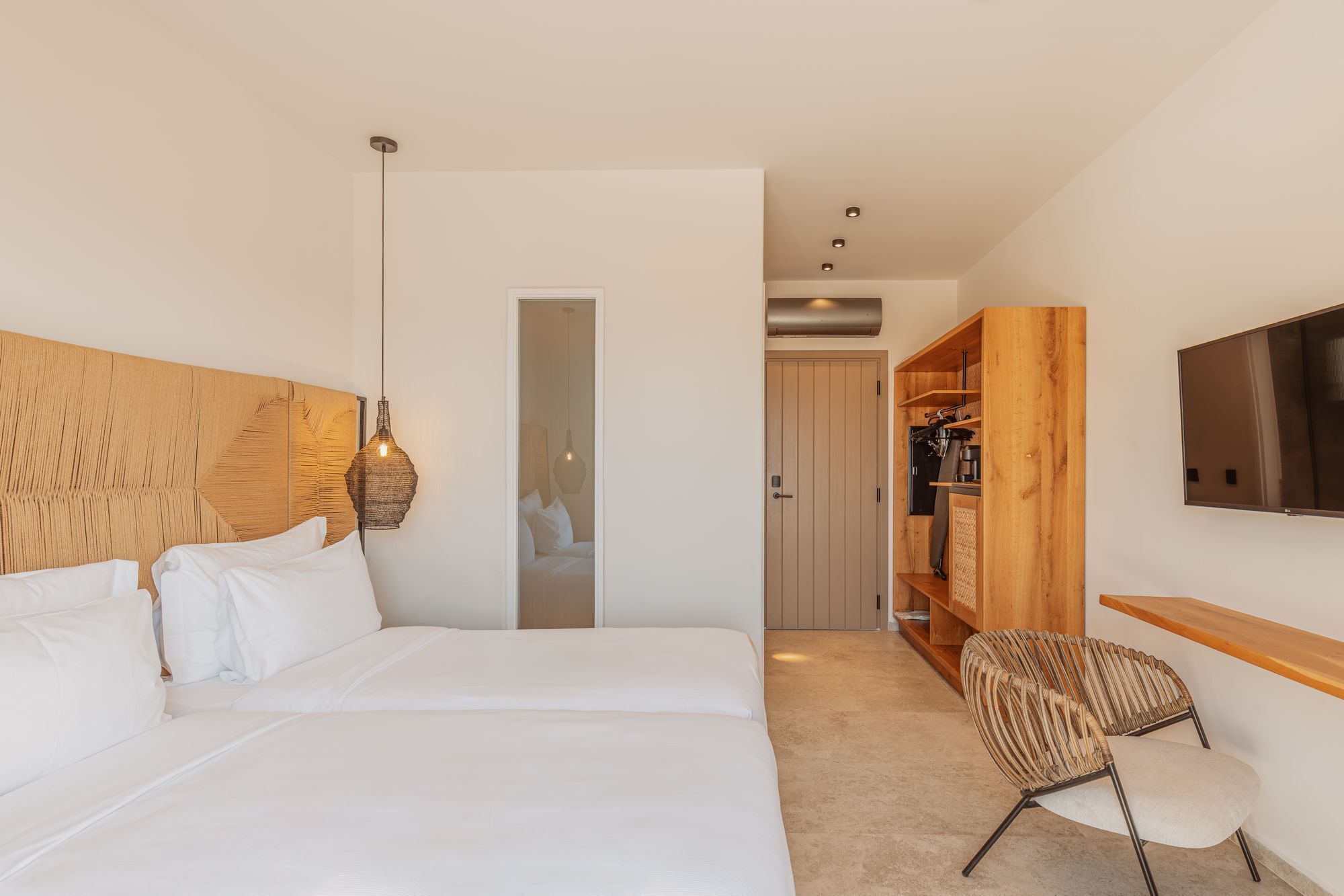 Hotelkamer met een groot bed, houten hoofdbord, hanglamp, kledingkast, een aan de muur bevestigde televisie en een stoel.