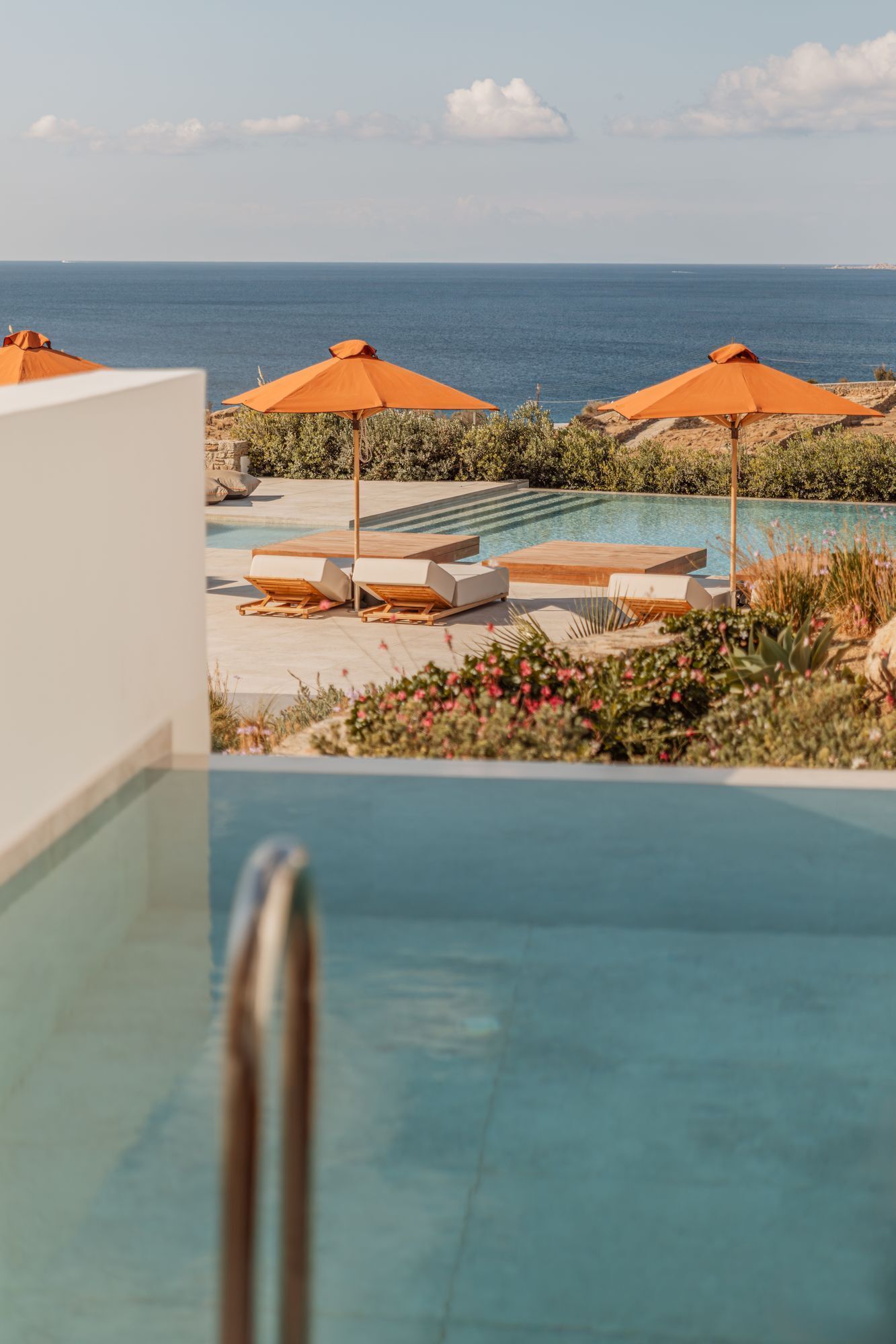 An infinity pool with a clear view of the ocean. There are lounge chairs and orange umbrellas.