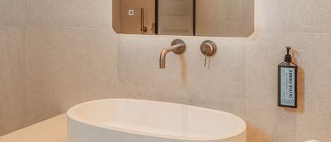 Un baño moderno con un lavamanos ovalado grande, un espejo y un perchero para toallas.