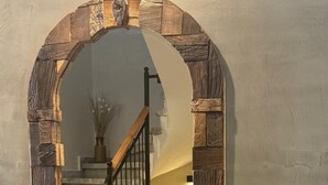 Una escalera con estructura de madera y barandilla negra, que conduce a una habitación con un florero de plantas secas.