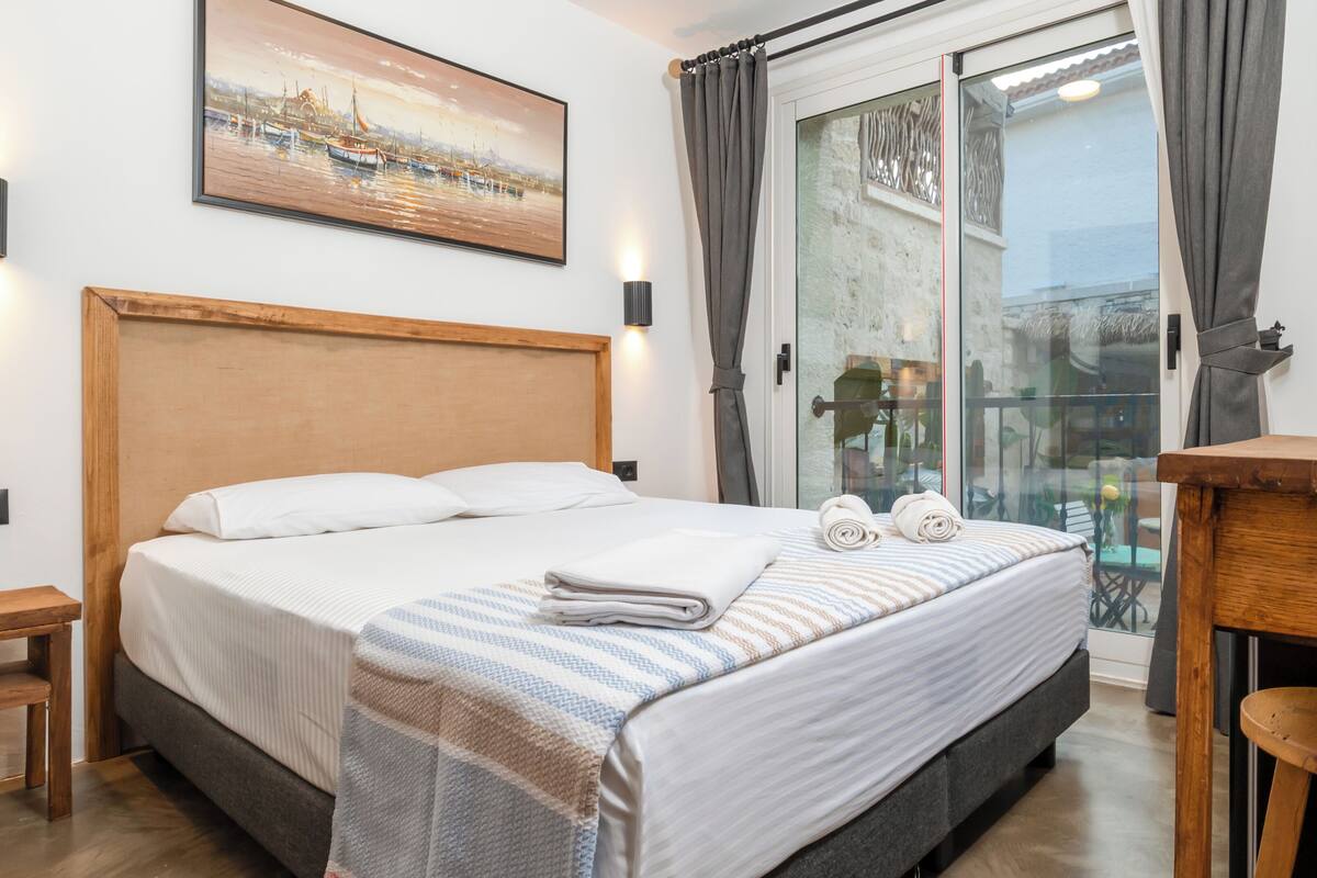 A hotel room with a large bed, a wooden headboard, a painting on the wall, and a balcony with a glass door.