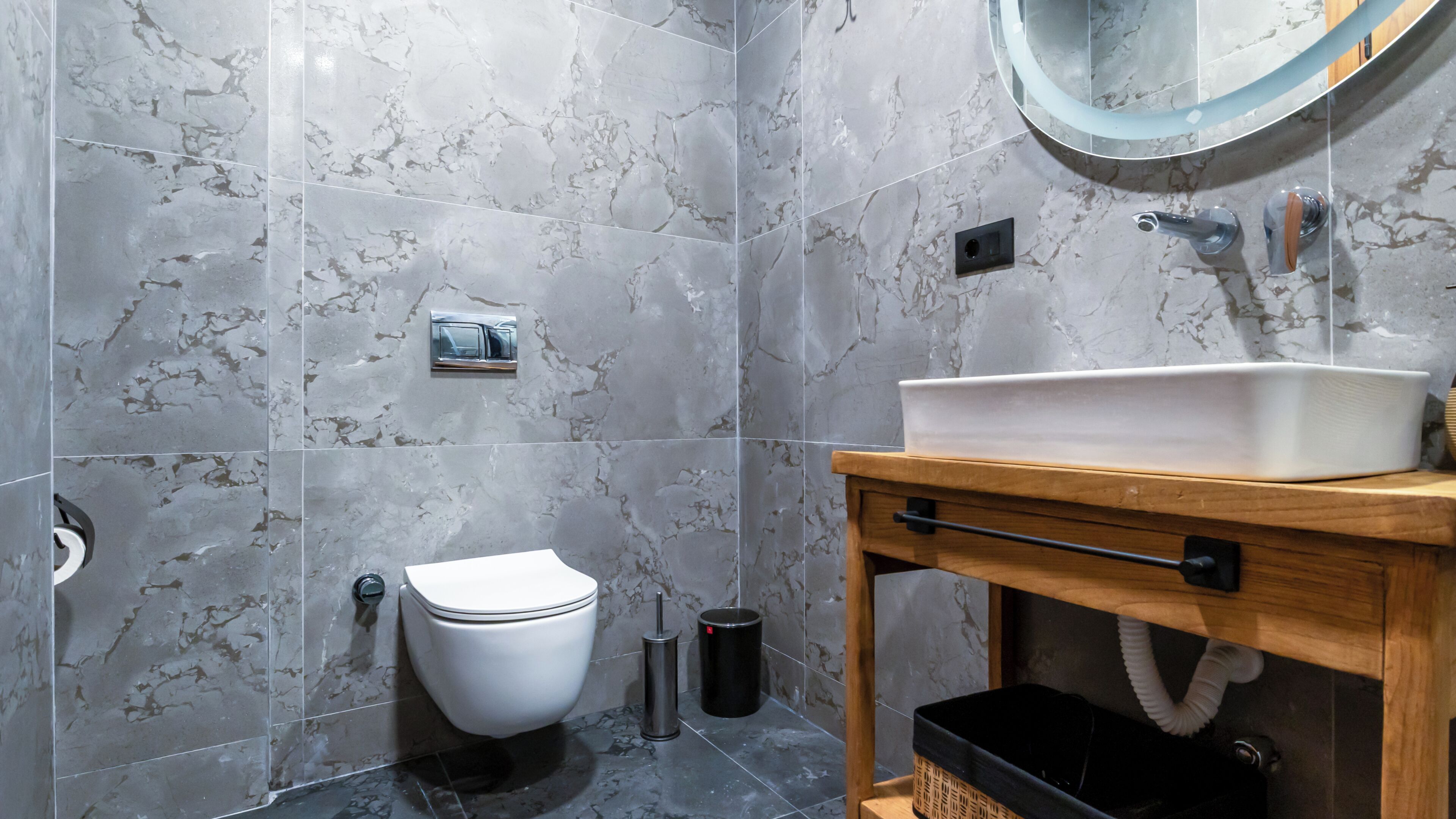 Un baño con inodoro, lavabo, espejo y paredes de mármol.