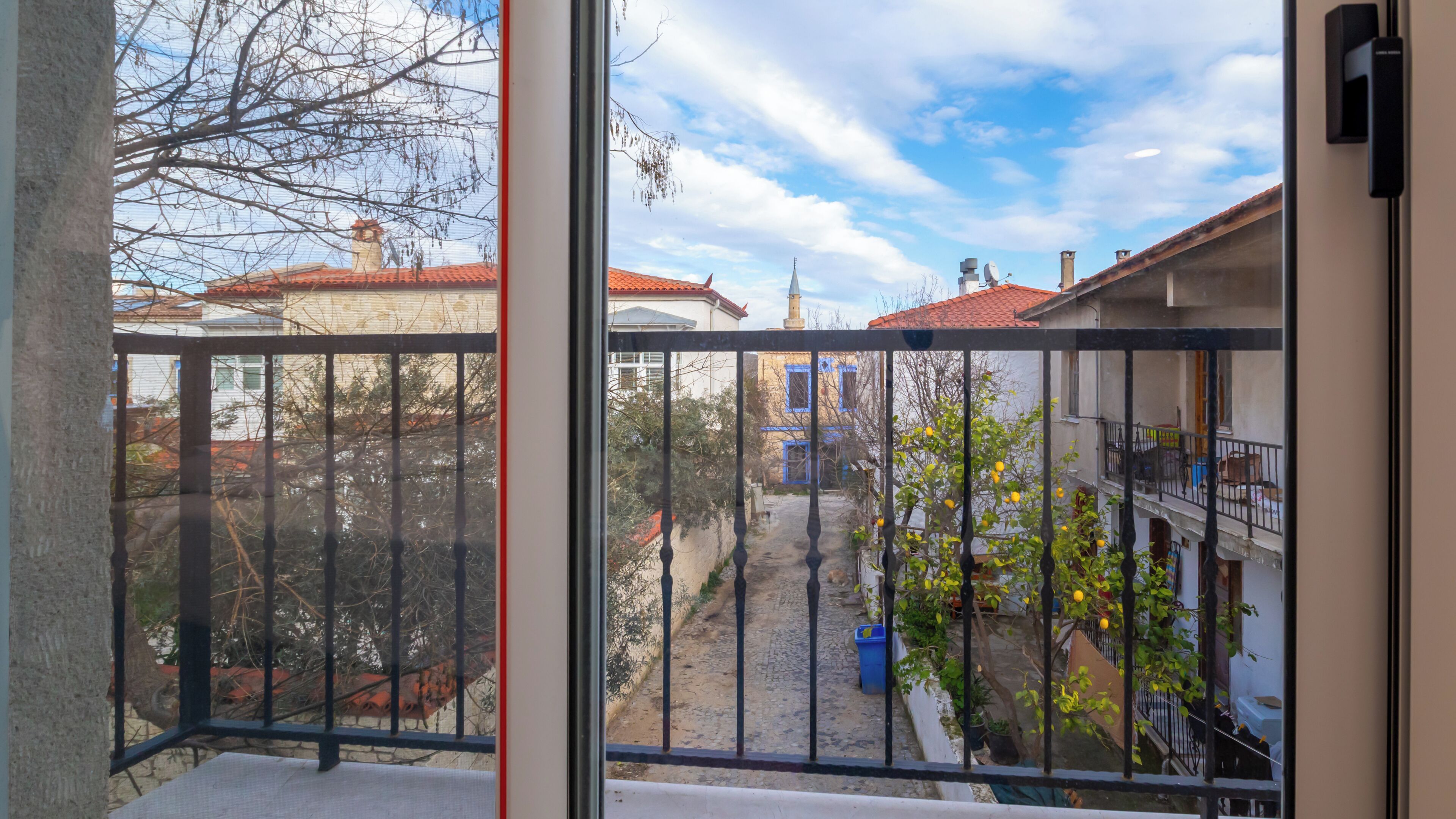 A balcony with a metal railing, a view of a courtyard with buildings, and a clear sky.