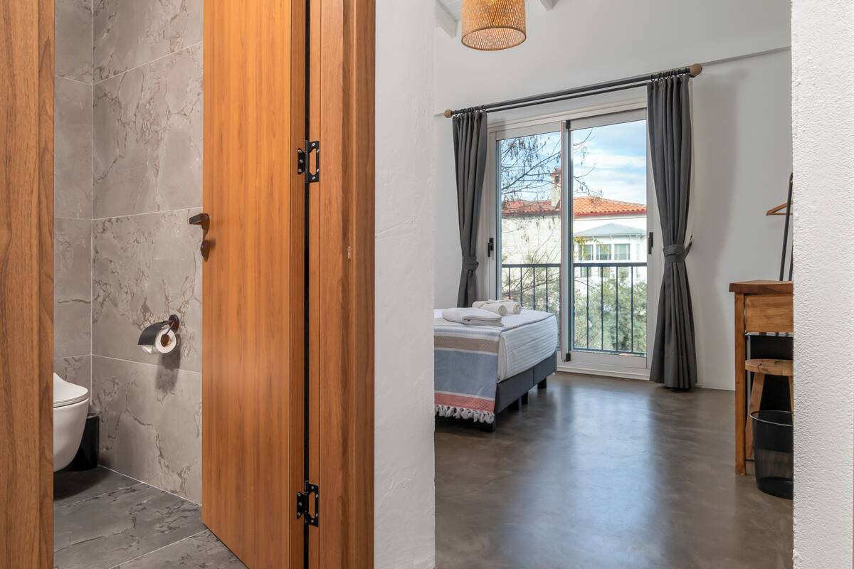 A bedroom with a bed, a window with curtains, a balcony, and a wooden door.