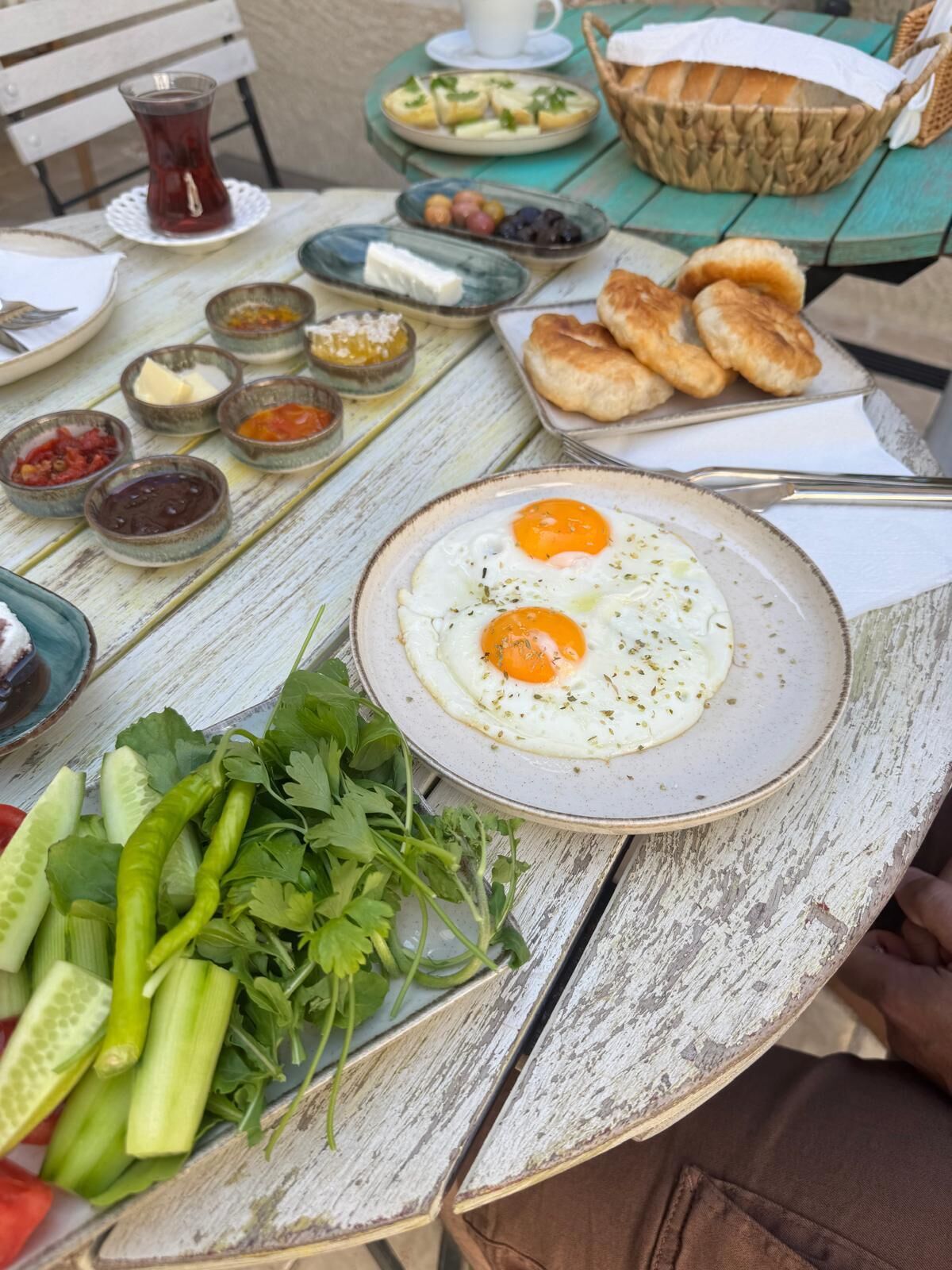 A table with a plate of eggs, various condiments, fresh vegetables, and bread.