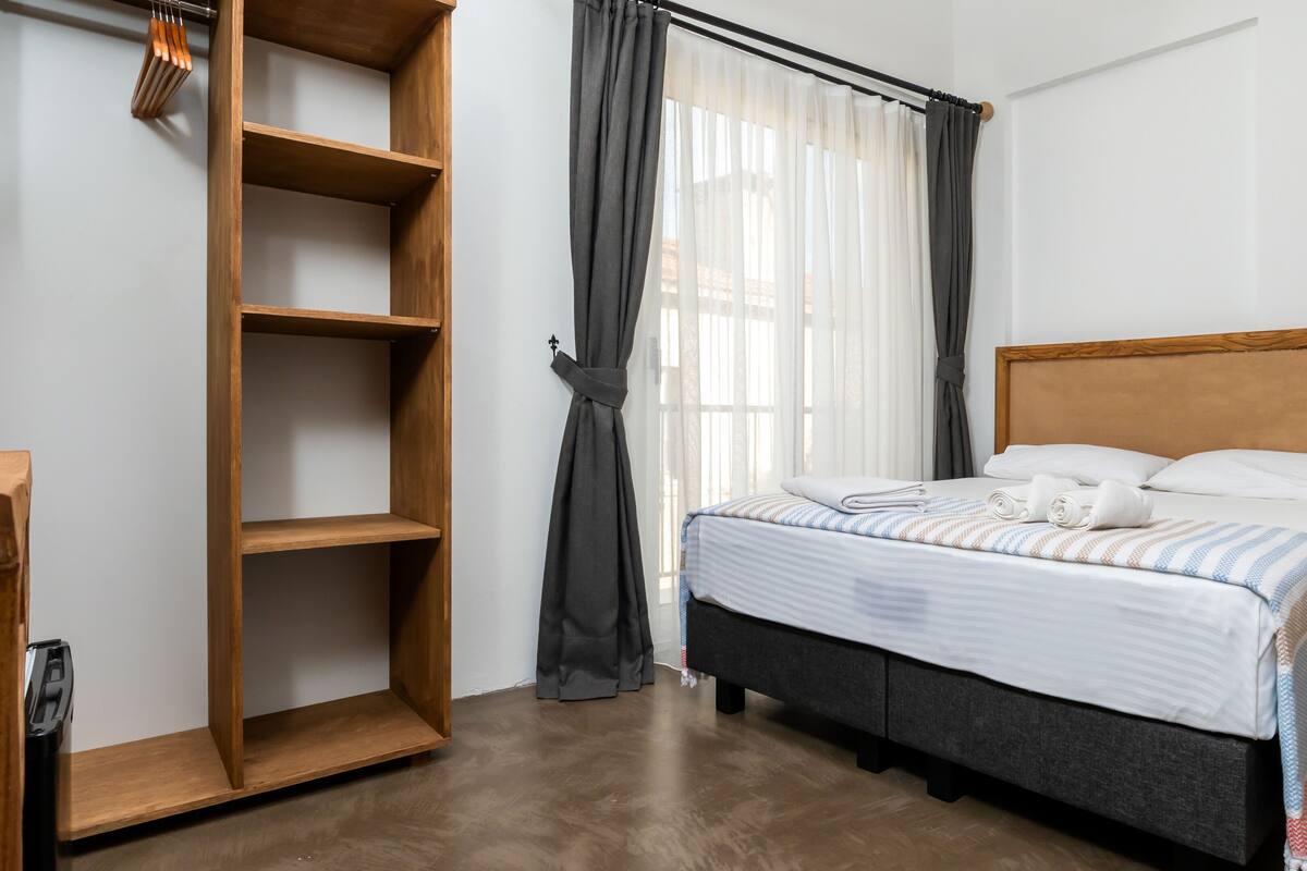 A neatly arranged bedroom with a bed, a wooden shelf unit, and a window with curtains.