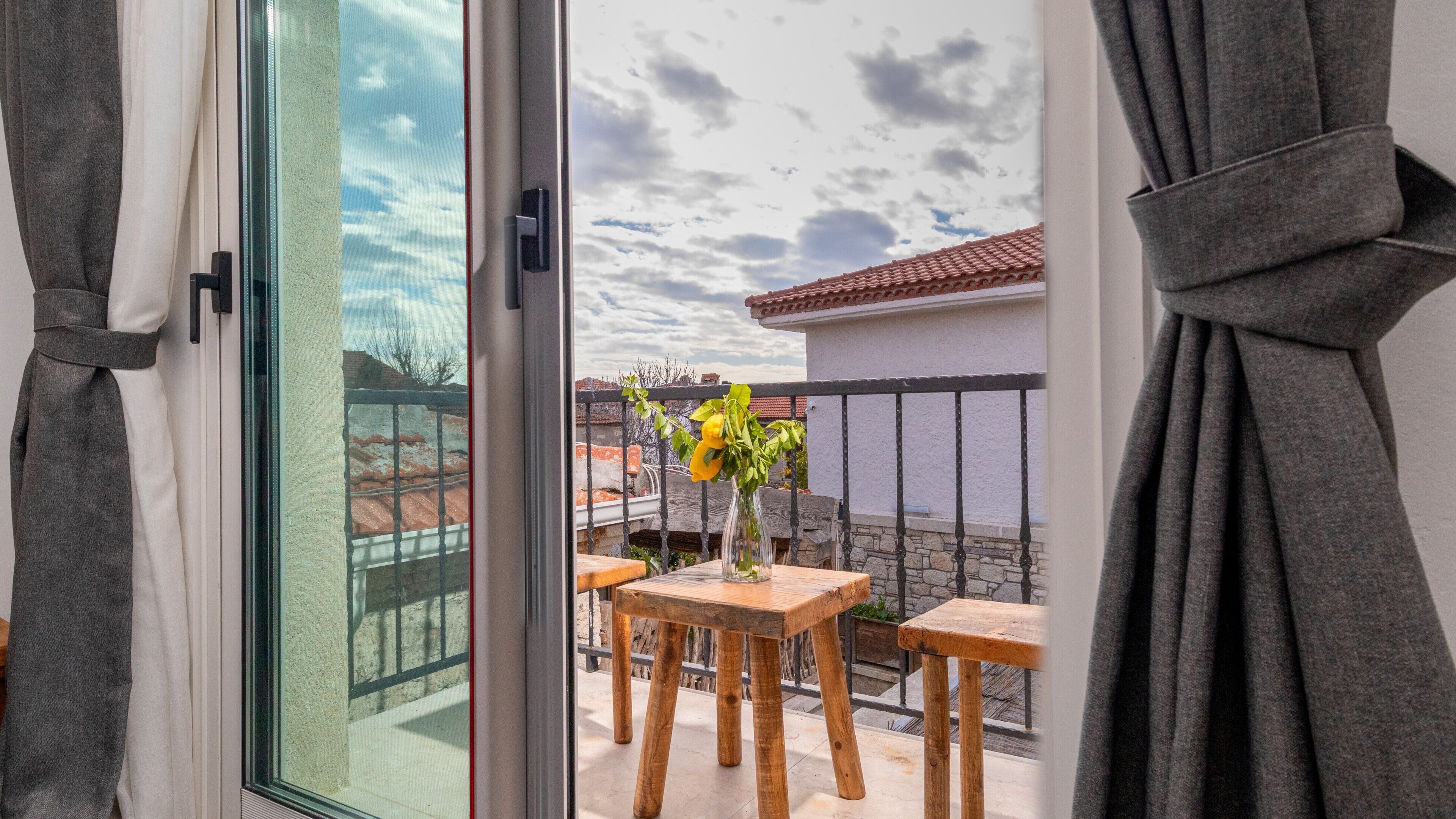 A balcony with a table and chairs, a vase with flowers, and a view of the sky and buildings.