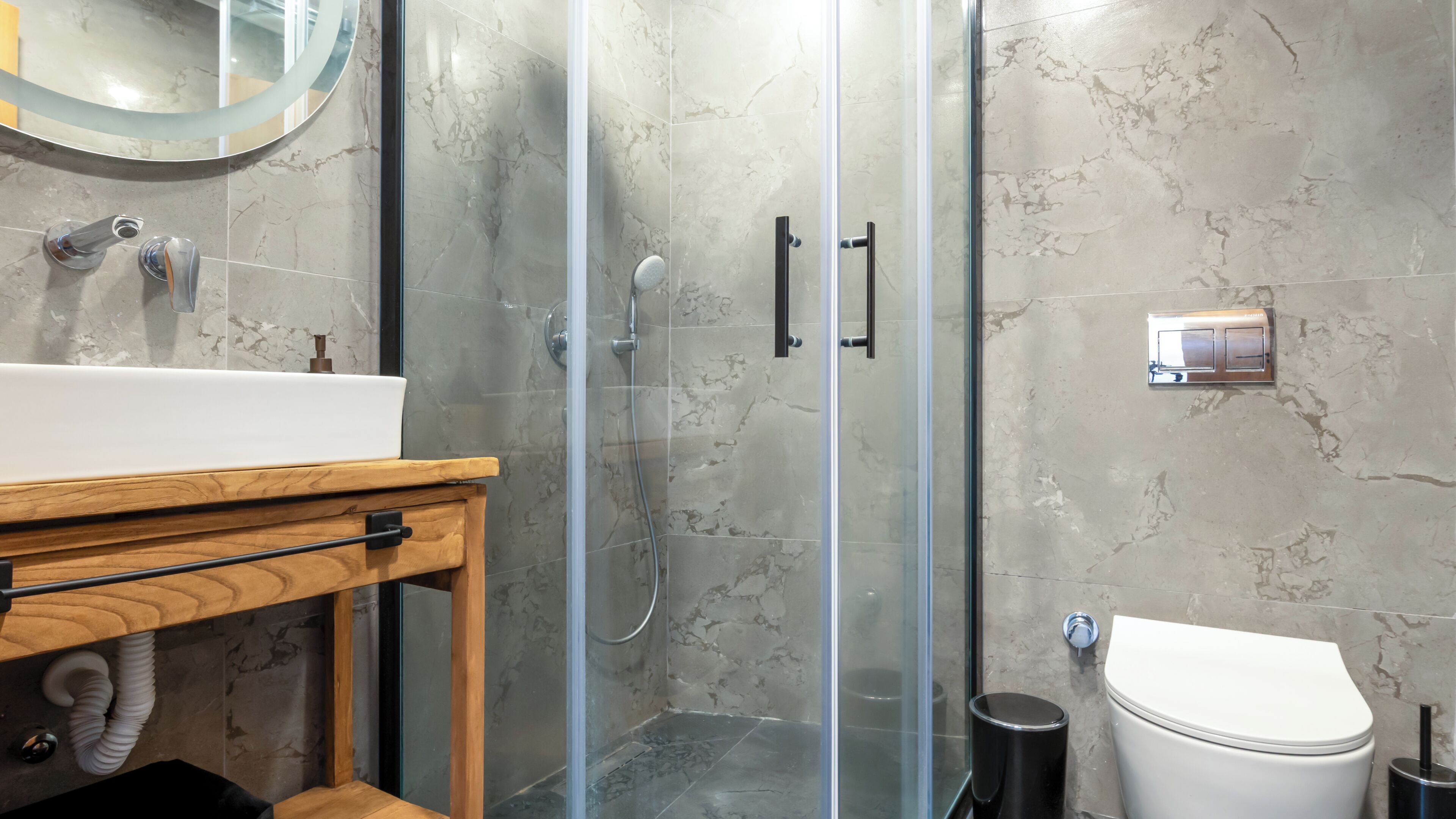 A modern bathroom with a glass-enclosed shower, a wooden vanity, a white sink, and a toilet.