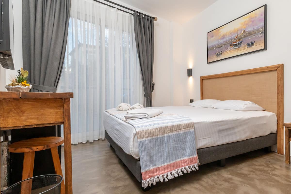 A modern hotel room with a bed, a desk, a chair, a small table, and a painting on the wall.