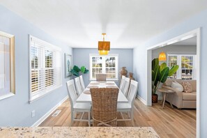 A dining area with a white table, wicker chairs, and a hanging light fixture.