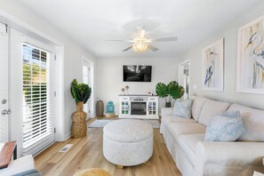 Un salon avec un canapé blanc, un pouf et un ventilateur de plafond.