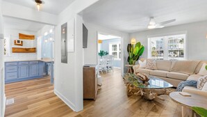 A modern living room with a glass coffee table, a sofa, and a dining area with white chairs. - The Beach Jewel - 100% Newly Renovated in 2024! (North Myrtle Beach)