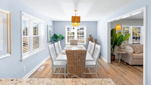 Un coin repas avec une table blanche, des chaises en osier et un luminaire suspendu.