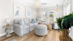 A modern living room with a sectional sofa, ottoman, and a large plant. - The Beach Jewel - 100% Newly Renovated in 2024! (North Myrtle Beach)