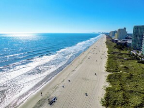 Une plage offrant une vue dégagée sur l’océan, une rive sablonneuse et des bâtiments en arrière-plan.