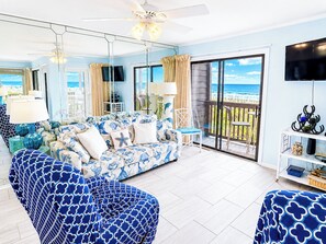 A living room with a sofa, chairs, a TV, and a balcony with a view.