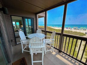 A balcony with a table and chairs, overlooking a beach with people and umbrellas.