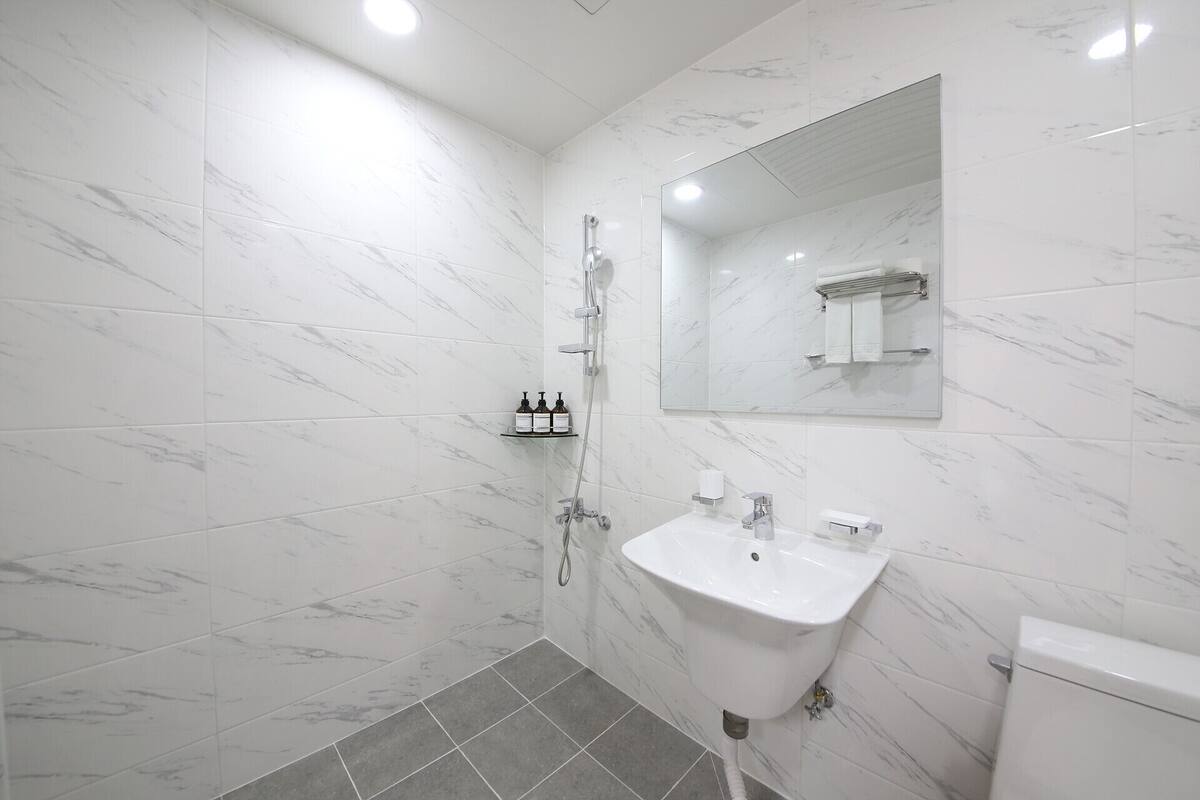 Un bany modern amb rajoles de marbre blanc, dutxa amb envàs de vidre, un lavabo blanc i un vàter.