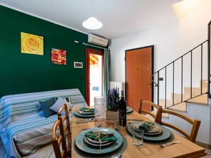 Een eetgedeelte met een houten tafel voor vier personen, een groene bank en een trap aan de rechterkant.