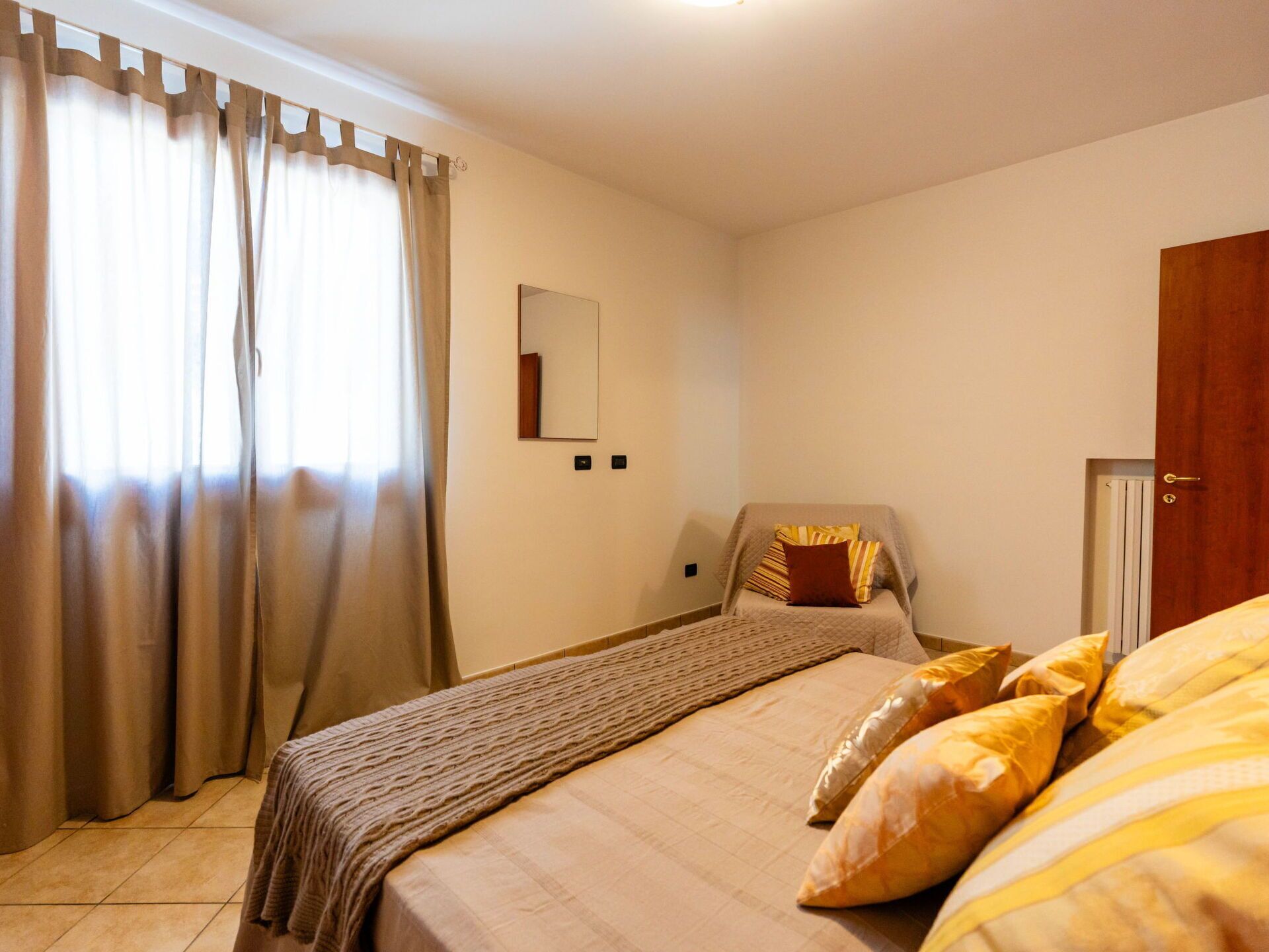 A bedroom with a bed, a chair, a mirror, and a door.